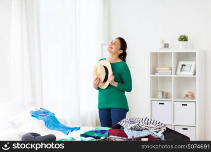 tourism, people and luggage concept - happy young woman with hat packing travel bag at home. happy woman with hat packing travel bag at home