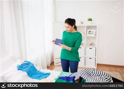 tourism, people and luggage concept - happy young woman with passport packing travel bag at home or hotel room