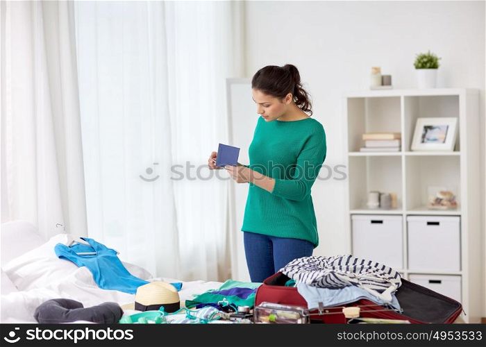 tourism, people and luggage concept - happy young woman with passport packing travel bag at home or hotel room. woman with passport packing travel bag at home