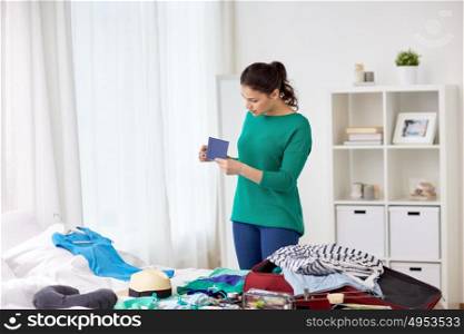 tourism, people and luggage concept - happy young woman with passport packing travel bag at home or hotel room. woman with passport packing travel bag at home