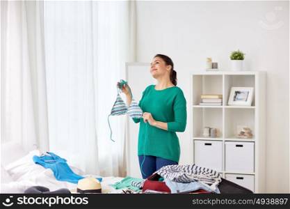 tourism, people and luggage concept - happy young woman with swimsuit packing travel bag at home. woman with swimsuit packing travel bag at home