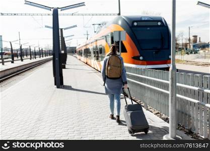 tourism, transportation and people concept - young woman in with travel bag and backpack walking along empty railway station. woman with travel bag on railway station