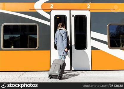 tourism, transportation and people concept - young woman with suitcase standing at train door at empty railway station. woman with suitcase at railway station
