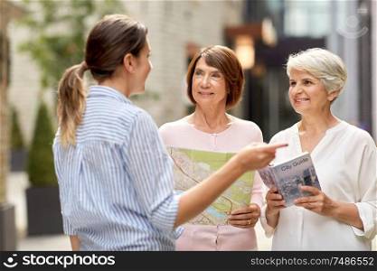 tourism, travel and friendship concept - female passerby showing direction to senior women with city guide and map on tallinn street. passerby showing direction to senior women in city