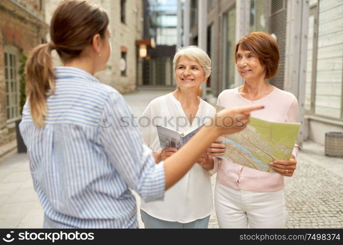 tourism, travel and friendship concept - female passerby showing direction to senior women with city guide and map on tallinn street. passerby showing direction to senior women in city