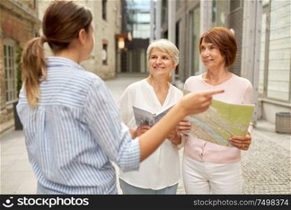 tourism, travel and friendship concept - female passerby showing direction to senior women with city guide and map on tallinn street. passerby showing direction to senior women in city