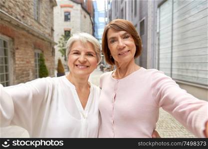 tourism, travel and friendship concept - happy senior women or friends taking selfie on street in tallinn. senior women or friends taking selfie in tallinn