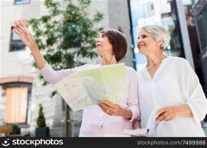tourism, travel and friendship concept - happy senior women with city guide and map on tallinn street. senior women with city guide and map on street