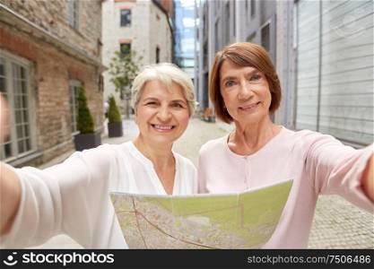 tourism, travel and friendship concept - happy senior women with city map taking selfie picture on street in tallinn. senior women with city map taking selfie outdoors