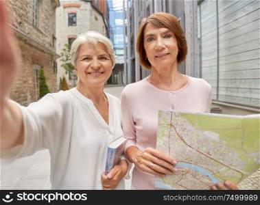 tourism, travel and friendship concept - happy senior women with map and city guide taking selfie on street in tallinn. senior women with map and city guide taking selfie