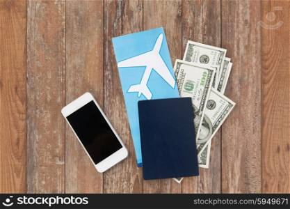 tourism, travel and objects concept - air ticket, money, smartphone and passport on wooden table background