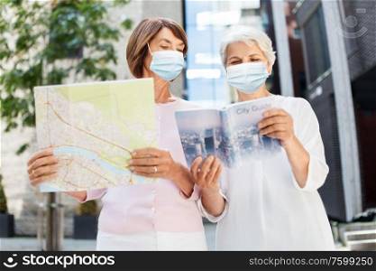 tourism, travel and pandemic concept - senior women in medical masks for protection from virus with city guide and map on tallinn street. senior women in masks with travel map in city