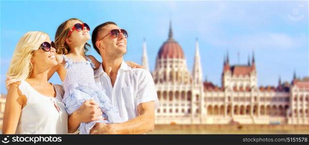 tourism, travel and people concept - happy family in sunglasses over house of parliament in budapest background. happy family over house of parliament in budapest