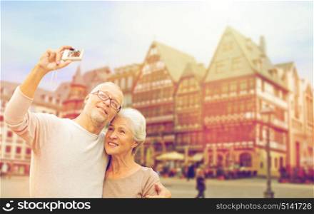 tourism, travel and people concept - happy senior couple with camera taking selfie over frankfurt am main city background. senior couple with camera traveling in frankfurt