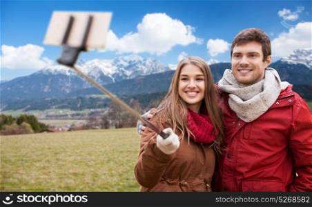 tourism, travel and people concept - happy smiling couple taking picture by smartphone selfie stick over alps mountains background. couple taking selfie by smartphone over alps