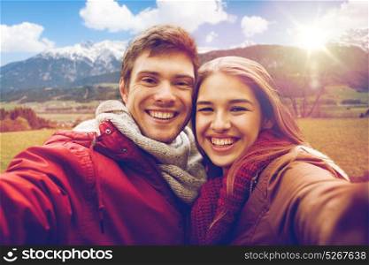 tourism, travel and people concept - happy smiling young couple taking selfie over alps mountains background. happy couple taking selfie over alps mountains