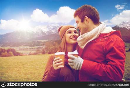 tourism, travel and people concept - happy young couple with coffee cups over alps mountains background. happy couple with coffee cups over alps mountains