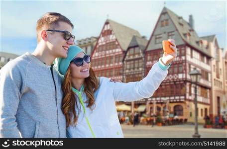 tourism, travel and people concept - smiling couple with smartphone taking selfie over frankfurt am main city street background. smiling couple with smartphone taking selfie