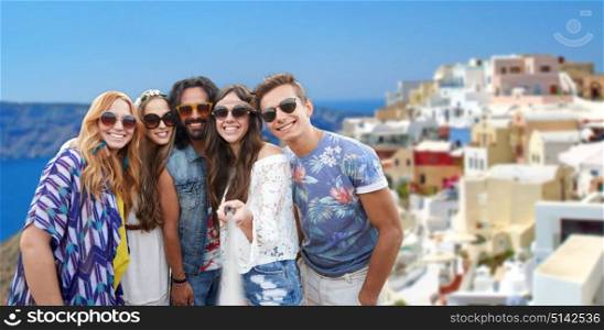 tourism, travel and people concept - smiling young hippie friends with selfie stick over oia town on santorini island background. happy hippie friends taking selfie on santorini