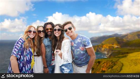 tourism, travel and summer holidays concept - smiling young hippie friends taking picture by selfie stick over big sur coast of california background. hippie friends taking picture by selfie stick. hippie friends taking picture by selfie stick