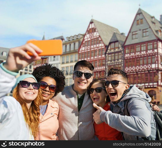 tourism, travel and technology concept - group of happy teenage friends taking selfie with smartphone over frankfurt am main city street background. friends taking selfie by smartphone in frankfurt