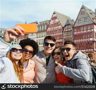 tourism, travel and technology concept - group of happy teenage friends taking selfie with smartphone over frankfurt am main city street background. friends taking selfie by smartphone in frankfurt