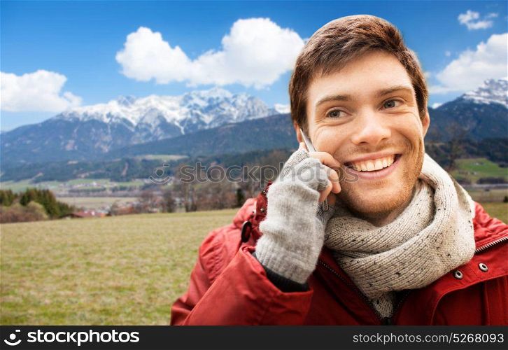 tourism, travel, communication and people concept - happy smiling young man calling on smartphone over alps mountains background. man calling on smartphone over alps mountains