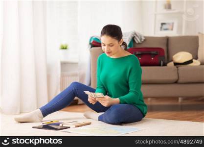 tourism, travel, finances and people concept - happy young woman with money, tablet pc computer and map at home