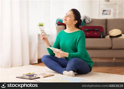 tourism, travel, finances and people concept - happy young woman with money, tablet pc computer and map at home
