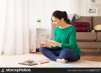 tourism, travel, finances and people concept - happy young woman with money, tablet pc computer and map at home. happy woman with money and travel map at home