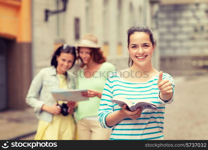 tourism, travel, holidays and friendship concept - smiling teenage girls with city guide, map and camera showing thumbs up outdoors