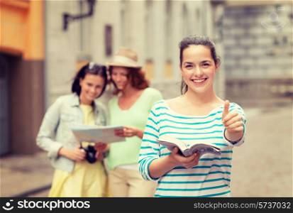 tourism, travel, holidays and friendship concept - smiling teenage girls with city guide, map and camera showing thumbs up outdoors