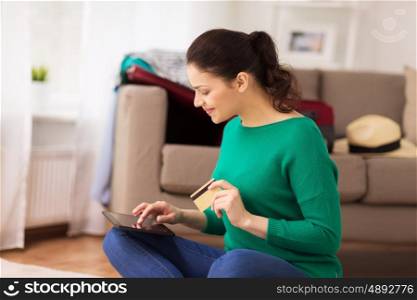 tourism, travel, insurance, payment and people concept - happy young woman with tablet pc computer and credit card at home going on trip