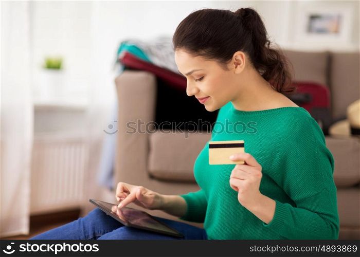 tourism, travel, insurance, payment and people concept - happy young woman with tabglet pc computer and credit card at home going on trip