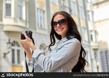 tourism, travel, leisure and holidays concept - smiling teenage girl with digital camera taking picture on city street