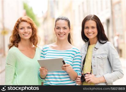 tourism, travel, leisure, holidays and friendship concept - smiling teenage girls with witch tablet pc computer and camera outdoors