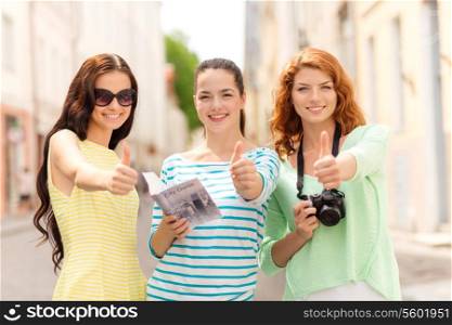 tourism, travel, leisure, holidays and friendship concept - smiling teenage girls with city guide and camera showing thumbs up outdoors