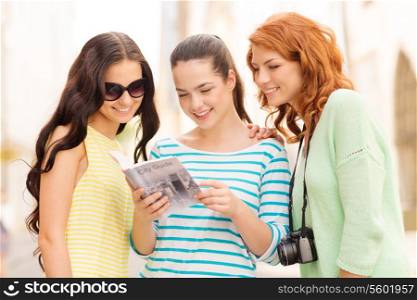 tourism, travel, leisure, holidays and friendship concept - smiling teenage girls with city guide and camera outdoors