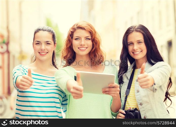 tourism, travel, leisure, holidays and friendship concept - smiling teenage girls with tablet pc computer and camera showing thumbs up