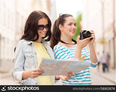 tourism, travel, leisure, holidays and friendship concept - two smiling teenage girls with map and camera outdoors