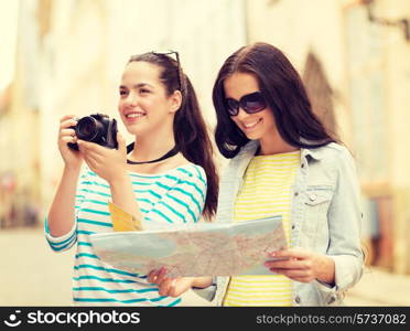 tourism, travel, leisure, holidays and friendship concept - two smiling teenage girls with map and camera outdoors