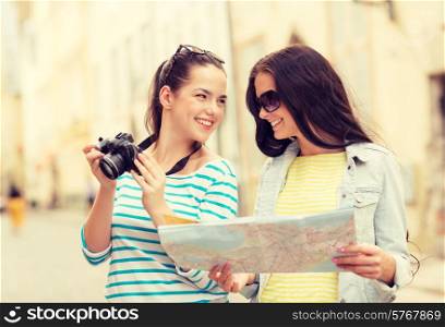tourism, travel, leisure, holidays and friendship concept - two smiling teenage girls with map and camera outdoors