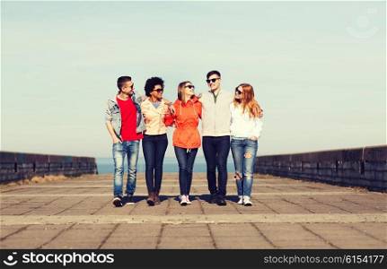 tourism, travel, people and friendship concept - group of happy teenage friends walking along city street and talking