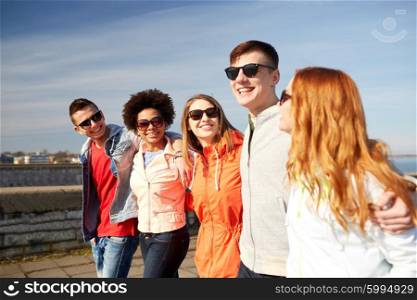 tourism, travel, people and leisure concept - group of happy teenage friends walking along city street and talking