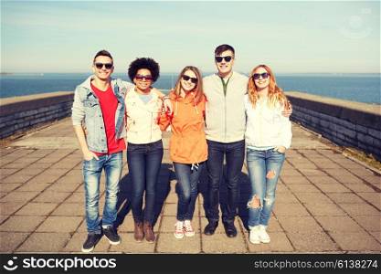tourism, travel, people and leisure concept - group of happy teenage friends in sunglasses hugging on city street