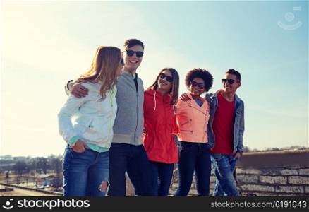 tourism, travel, people and leisure concept - group of happy teenage friends walking along city street and talking