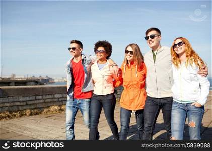 tourism, travel, people and leisure concept - group of happy teenage friends walking along city street