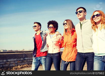 tourism, travel, people and leisure concept - group of happy teenage friends walking along city street