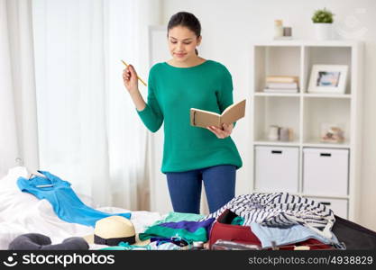 tourism, travel, people and luggage concept - happy young woman with notebook planning her trip at home. woman with notebook planning her trip at home