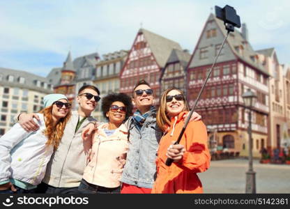 tourism, travel, people and technology concept - group of smiling teenage friends taking selfie with smartphone and monopod over frankfurt am main city street background. friends taking photo by selfie stick in frankfurt